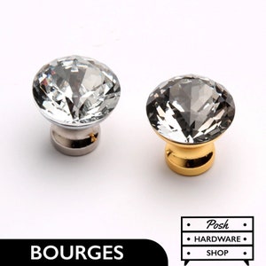Op de afbeelding: Twee kristallen kastknoppen, een met een zilveren basis en een met een gouden basis. De knoppen zijn rond en hebben een facetgeslepen ontwerp.