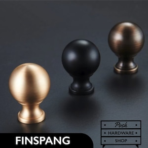 May include: Three round cabinet knobs in different finishes: gold, black, and bronze. The knobs have a spherical shape with a slightly raised base.