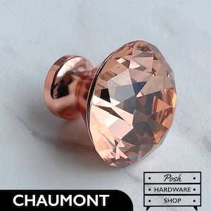 May include: Rose gold cabinet knob with a faceted crystal design. The knob has a round base and a faceted crystal top.