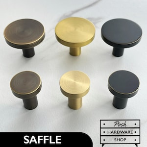 May include: Six cabinet knobs in three different finishes: antique brass, polished brass, and black. The knobs are round with a flat top and a short, cylindrical base.