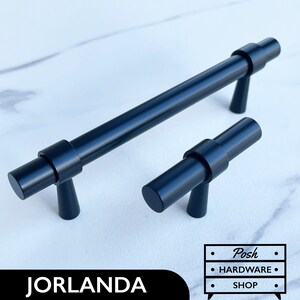 Può includere: Due maniglie per mobili in metallo nero, una lunga e una corta, con forma cilindrica e design a T. Le maniglie hanno una finitura opaca.