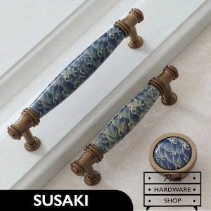 May include: Two antique gold cabinet pulls with a blue and white floral design. The pulls are 12.7 cm long. The image also shows a matching knob.