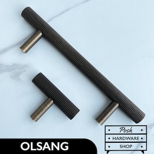 May include: Two black cabinet pulls with a ribbed texture. The larger pull is 12.7 cm long and the smaller pull is 7.6 cm long. Both pulls have a brushed brass finish.