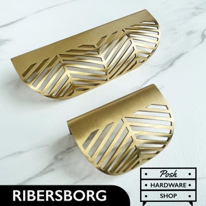 Op de afbeelding: Twee gouden metalen kastgrepen met een geometrisch bladontwerp. De grepen zijn halfrond en hebben een geborstelde afwerking.