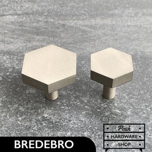 May include: Two silver hexagonal cabinet knobs with a brushed finish. The larger knob is on the left and the smaller knob is on the right.