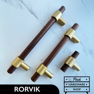 May include: Three wooden cabinet pulls with gold metal accents. The pulls are in different sizes. The largest pull is 12 inches long. The middle pull is 8 inches long. The smallest pull is 3 inches long. The pulls are made of walnut wood and have a brushed gold finish.
