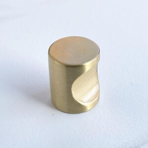 May include: A brushed gold cabinet knob with a unique curved design.