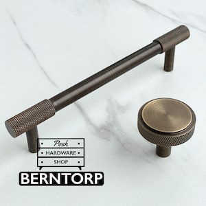 May include: A dark bronze cabinet handle with a knurled texture on the ends and a matching round cabinet knob with a knurled edge and a smooth center. The image includes a logo with the text Posh HARDWARE SHOP and BERNTORP.