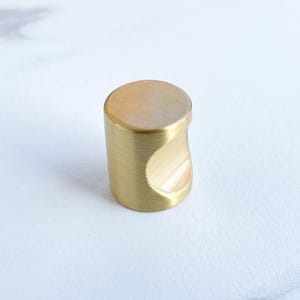May include: A gold-toned cabinet knob with a rounded, cylindrical shape and a cut-out for a finger pull.