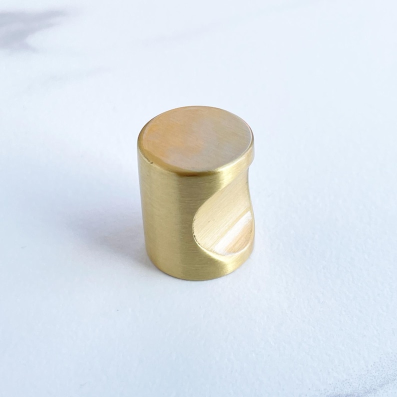 May include: A gold-toned cabinet knob with a rounded, cylindrical shape and a cut-out for a finger pull.