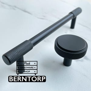 May include: A matte black cabinet handle and a matching round cabinet knob, both featuring a textured knurled pattern on the ends and sides. The image includes a logo with the text Posh HARDWARE SHOP and the word BERN TORP at the bottom.