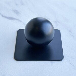 May include: A black sphere sits on a black square base. The sphere is smooth and glossy.