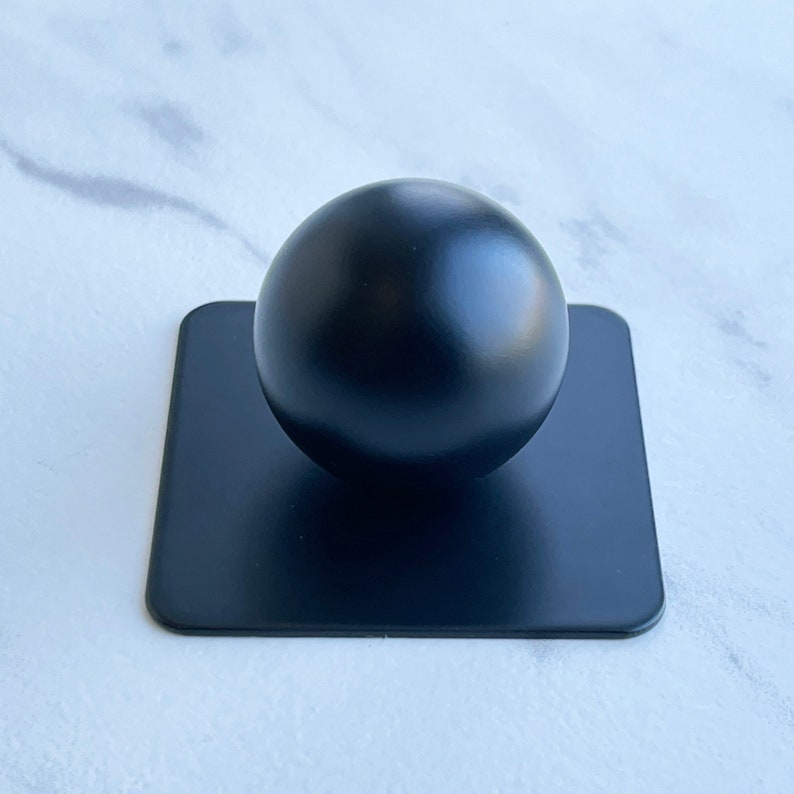 May include: A black sphere sits on a black square base. The sphere is smooth and glossy.