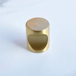 May include: A gold-toned cylindrical cabinet knob with a rounded top and a cutout on the front.