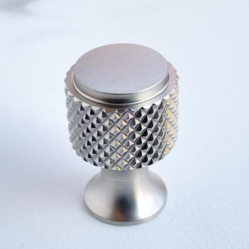 May include: A brushed nickel cabinet knob with a diamond-patterned grip. The knob has a circular top and a rounded base, suitable for drawers or cabinet doors. The hardware is made of metal.