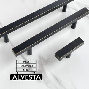 May include: Three matte black cabinet pulls with gold-toned edges, featuring two long bar handles and one short T-bar knob. A logo graphic is present with the text Posh HARDWARE SHOP and ALVESTA in a black rectangle at the bottom left corner.