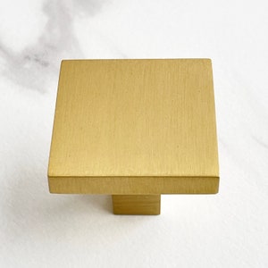 Op de afbeelding: Een vierkante kastknop met een geborstelde gouden afwerking.
