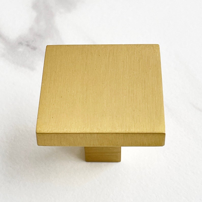 Op de afbeelding: Een vierkante kastknop met een geborstelde gouden afwerking.