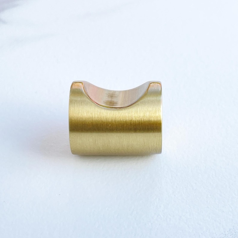 May include: A brushed gold cabinet knob with a rounded, curved top. The knob is made of metal and has a smooth, polished finish.