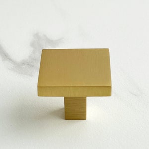 Op de afbeelding: Een vierkante kastknop van geborsteld goud met een rechthoekige basis.