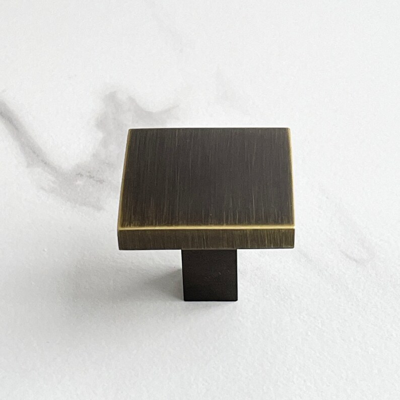 Op de afbeelding: Een vierkante kastknop met een geborsteld messing afwerking en een zwarte basis.