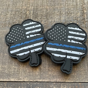 May include: Two black, distressed, shamrock-shaped patches with a thin blue line and an American flag design.