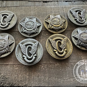 Op de afbeelding: Acht verschillende metalen challenge-munten met verschillende ontwerpen. Sommige munten hebben een ster met de woorden "Veiligheid, Service, Beveiliging" en "California Highway Patrol" rond de ster. Andere munten hebben een gevleugelde "C" met de woorden "California Highway Patrol" en "Eerlijkheid, Professionaliteit, Integriteit, Moed, Toewijding, Dapperheid" rond de "C".