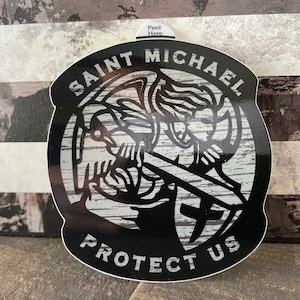 May include: Black and white sticker featuring a detailed illustration of Saint Michael, holding a sword and shield. The text "Saint Michael Protect Us" is displayed in a bold, white font. The sticker has a wood grain background and a "Peel Here" tab.