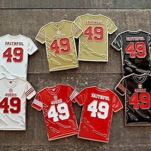 Puede incluir: Seis pines de esmalte de camisetas de fútbol. Las camisetas son de diferentes colores, incluyendo oro, blanco, negro y rojo. Cada camiseta tiene el número 49 en la espalda y las palabras "Faithful" y "49ers" en el frente.
