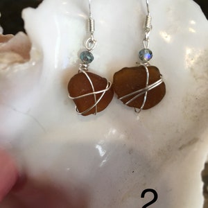 May include: A pair of earrings featuring brown sea glass wrapped in silver wire with a small blue crystal bead on each earring.
