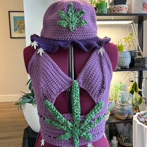 May include: Purple crocheted top with a green marijuana leaf design and matching purple crocheted hat with a green marijuana leaf design.