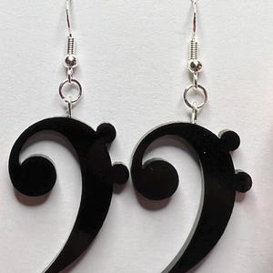 May include: A pair of black bass clef earrings. Each earring features a glossy black bass clef shape suspended from a silver-colored ear wire. The earrings are designed for pierced ears and are suitable for music lovers.