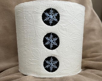May include: A white paper towel roll with three black circles with blue snowflake designs on the front.