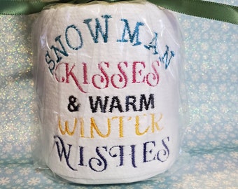 May include: A white toilet paper roll with the text "Snowman Kisses & Warm Winter Wishes" embroidered in colorful thread.