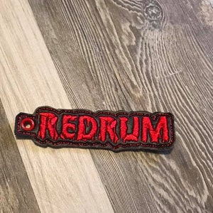 May include: A black and red embroidered key chain with the word "REDRUM" in red.