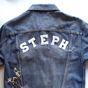 May include: A blue denim jacket with the name "STEPH" in white letters on the back.