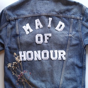 May include: A blue denim jacket with white felt letters that spell "Maid of Honour" on the back.