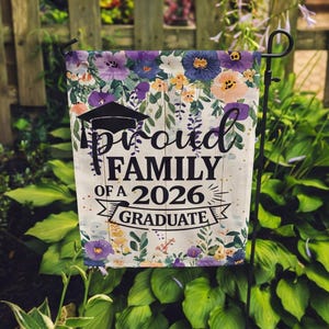 May include: A garden flag with a floral border in shades of purple, blue, and peach. The flag features the text "Proud Family of a 2026 Graduate" in black, with a graduation cap graphic. The flag is displayed on a black metal stand.