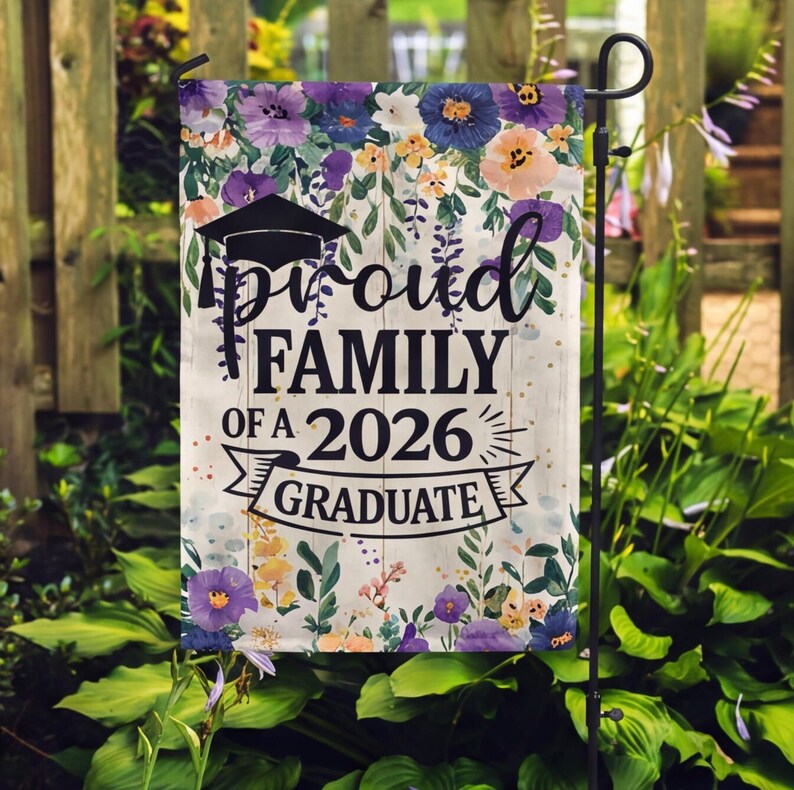 May include: A garden flag with a floral design and the text "Proud Family of a 2026 Graduate." The flag features a graduation cap and a banner. The flowers are in shades of purple, yellow, and peach.