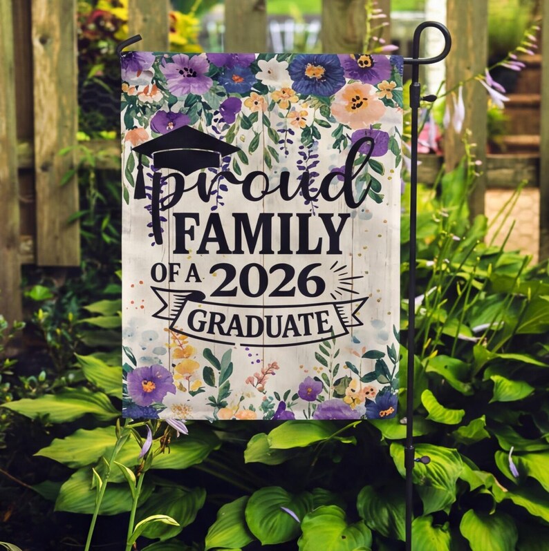 May include: A garden flag with a floral design and the text "Proud Family of a 2026 Graduate." The flag features a graduation cap and a banner. The flowers are in shades of purple, yellow, and orange.