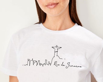 Puede incluir: Camiseta blanca con un dibujo de línea negra de la estatua del Cristo Redentor en Río de Janeiro, Brasil. El dibujo también incluye un horizonte de la ciudad y el texto "Río de Janeiro".