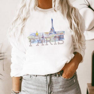May include: White sweatshirt with a watercolor illustration of the Eiffel Tower and the word "PARIS" printed in pink.