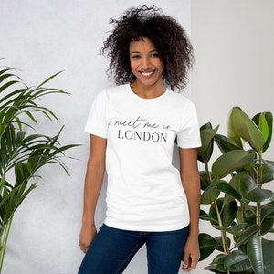 May include: White t-shirt with black text that reads "meet me in LONDON". A person is wearing the t-shirt.