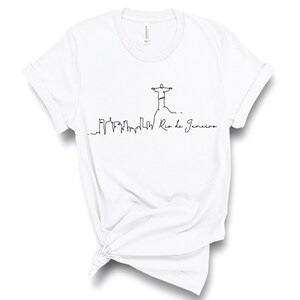 May include: White t-shirt with a black line drawing of the Christ the Redeemer statue in Rio de Janeiro, Brazil. The drawing also includes a skyline of the city and the text "Rio de Janeiro".
