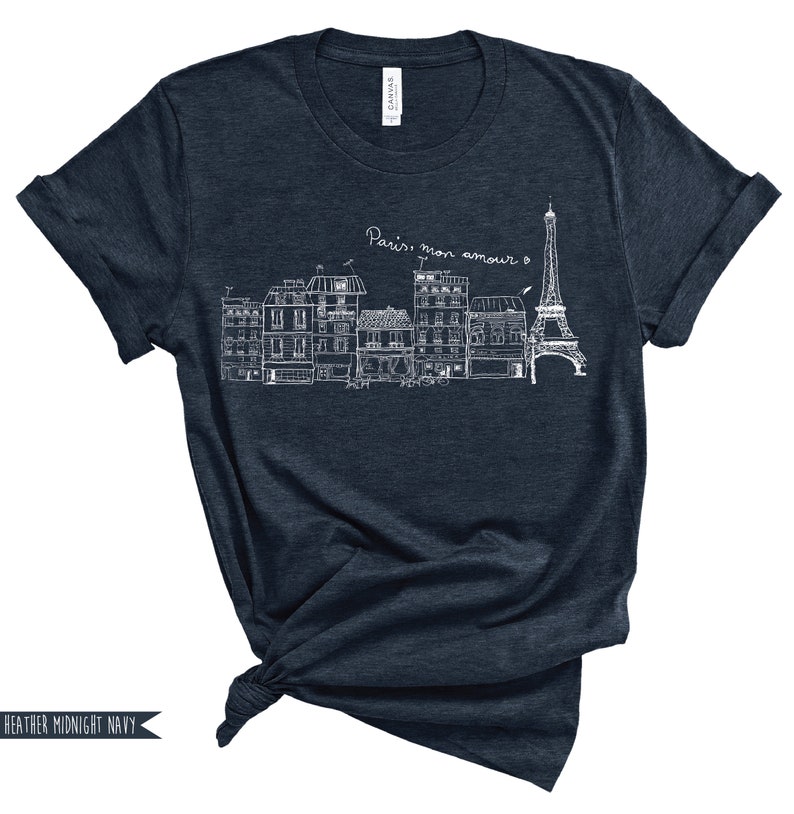 May include: A dark blue t-shirt with a white graphic of the Eiffel Tower and Parisian buildings. The text "Paris, mon amour" is written above the graphic.