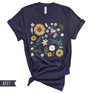 May include: Navy blue t-shirt with a floral print featuring sunflowers, daisies, and other wildflowers in shades of yellow, white, and blue.