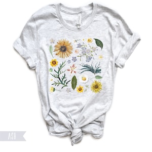 May include: A heather grey t-shirt with a floral print featuring sunflowers, daisies, and other wildflowers in shades of yellow, white, and blue.