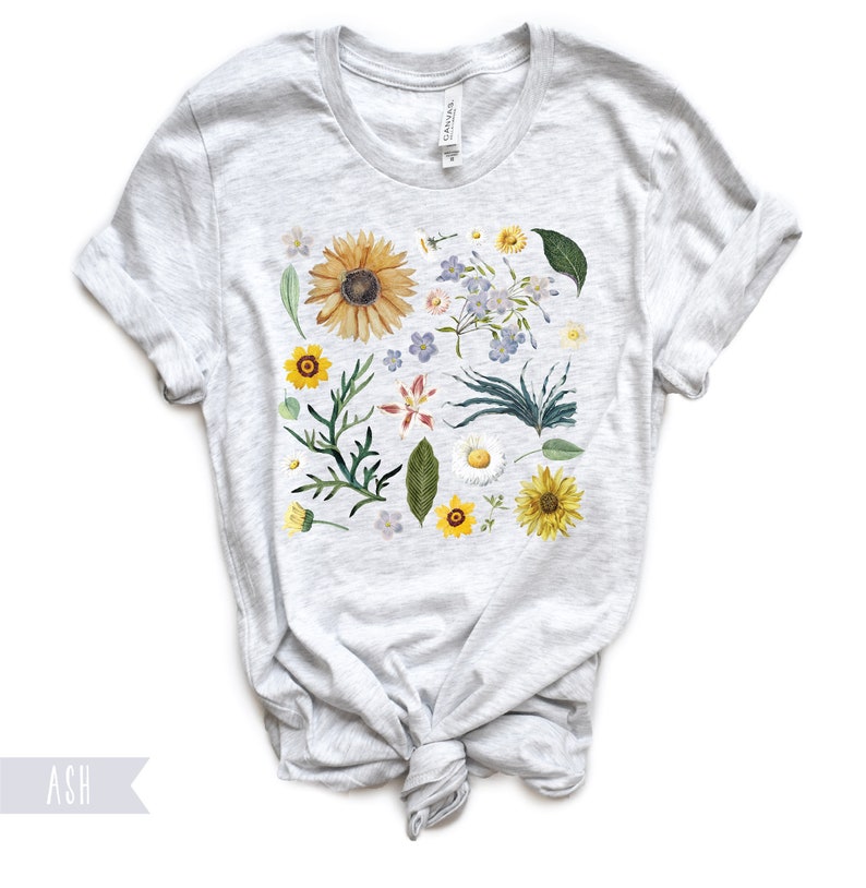 May include: A heather grey t-shirt with a floral print featuring sunflowers, daisies, and other wildflowers in shades of yellow, white, and blue.