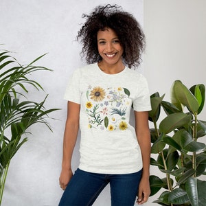 May include: A white t-shirt with a floral print featuring a variety of flowers and leaves in shades of yellow, blue, green, and pink.