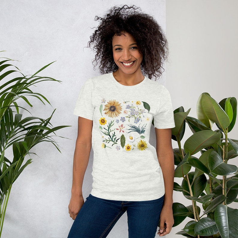 May include: A white t-shirt with a floral print featuring a variety of flowers and leaves in shades of yellow, blue, green, and pink.
